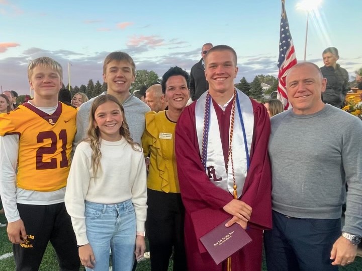 Jill with her family at a Forest Lake graduation, son in maroon and gold cap and gown, on the field at sunset